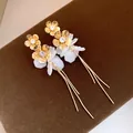 Vue détaillée d'élégantes boucles d'oreilles à pampilles dorées avec pétales en résine. - Style fleur à pompons / Or