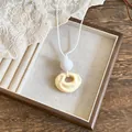 Close-up detail view of the pleated resin pendant on a minimalist white cord necklace. - Yellow