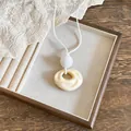 Close-up of minimalist cream resin wrinkled circle pendant with white leather cord - Beige
