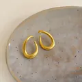 Detailed macro shot of minimalist gold twisted oval hoop earrings on a ceramic plate. - Silver Earring Post Style / Gold