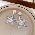 Close-up of silver textured starfish drop earrings on a vintage beige ceramic plate. - Earrings / Silver