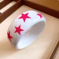 Detailed close-up of a white resin bangle featuring vibrant pink star patterns on a tray. - White-Rose Red