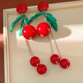 Primo piano di orecchini a ciliegia rossi con foglie verdi e lunghe nappe argentate su box. - Stile Nappina Ciliegia / Rosso-Verde