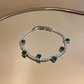 Sparkling silver bracelet with green round zircons displayed on golden reflective tray. - Round Tennis Chain / Green