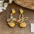 Detail view of yellow fabric flower tassel earrings with colorful beads on wooden surface - Yellow