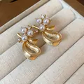 Detailed macro view of elegant gold-finished bow earrings adorned with pearls and crystals. - Stud Earrings / Gold