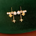 Dettaglio di orecchini dorati con fiori, stelle, perle e zirconi incastonati a mano. - Oro