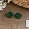 Detailed view of green glass beaded flower stud earrings on a rustic wooden background. - Green