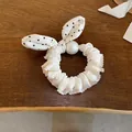 Detail view of the elegant white polka dot bow hair scrunchie featuring a large pearl - White