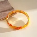 Vista detallada de los patrones de esmalte naranja y amarillo en brazalete dorado - Amarillo-Naranja