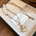Close-up detail of a white nautilus shell pendant necklace on a brown cord for beach resort style - Shell / Coffee
