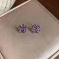 Detailed macro view of purple flower-shaped zircon stud earrings on a beige jewelry box - Purple