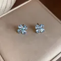 Close-up detail of elegant light blue zircon flower stud earrings on a beige texture - Blue