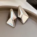 Nahaufnahme von silbernen geometrischen Ohrsteckern mit glänzender Metalloberfläche. - Unregelmäßiger Geometrischer Stil / Silber