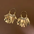 Detailed macro view of gold sequined tassel hoop earrings on brown background - Sequin Tassel Style / Gold