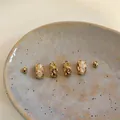 Close-up detail of elegant gold-tone earring set with white stones on a ceramic plate - 3# Cat's Eye/Quilted Style