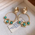 Nahaufnahme von goldenen Creolen mit floralem Design und türkisfarbenen Perlen - Reifen Blumen Stil / Gold-Blau