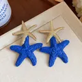 Close-up detail of blue raffia woven starfish and gold metal stud earrings for summer resort - Single Starfish Style (HE31348) / Gold + Blue