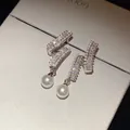 Close-up of elegant silver needle earrings with shimmering zircons and dangling pearls - Pearl Pendant Style / Silver