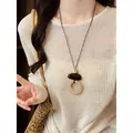 Bohemian woven necklace with circular pendant on a model wearing cream knit top - Round Woven Style (HN12226) / Brown