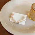 Close-up of U-shaped pearl earrings featuring white and pink pearls on display card - White-Pink-Brown