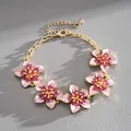Close-up detail of a gold-tone metal bracelet with five pink and white enamel flowers - Pink