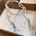 Detailed view of long pearl necklace featuring rhinestone bows and chain tassels. - Bow Tassel / Silver-Beige