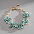 Detail shot of an elegant gold-tone metal bracelet featuring blue enamel flowers - Blue