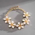 Detailed view of gold chain bracelet with five white enamel flower charms on grey leather - White