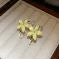 Primer plano de pendientes de aro con flores de resina amarilla con purpurina en caja - Amarillo