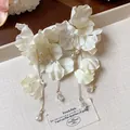 Detailed view of white fabric flower earrings with gold tassels and delicate pearls. - Flower Tassel Style / White