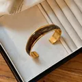 Dettaglio ravvicinato di un bracciale rigido dorato ondulato con smalto marrone - Cuff Bracelet / Marrone