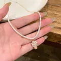 Dettaglio del ciondolo a cesto di fiori in zircone su un elegante collana di perle doppia - Stile Ciondolo Cesto di Fiori / Oro