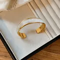 Primo piano di un bracciale rigido dorato ondulato con design in smalto marmorizzato - Cuff Bracelet / Bianco