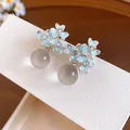 Close-up of light blue resin flower stud earrings with crystals and round beads. - Blue