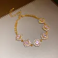 Gros plan d'un bracelet doré avec des fleurs en zircon rose et des cristaux brillants - Style Fleur / Or-Rose