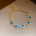 Gros plan d'un bracelet doré élégant avec cinq breloques fleurs en zircon bleu radiant - Style Fleur / Or-Bleu