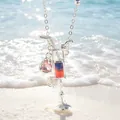 Detailansicht einer silbernen Cocktailglas-Halskette mit rosa Edelstein am Strand. - Rosa