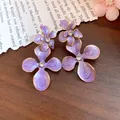 Detail view of purple enamel flower earrings with central rhinestones on a wooden background. - Purple