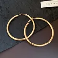 Close-up detail view of elegant large gold-finish hoop earrings with a polished surface. - Gold