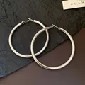 Close-up of large polished silver hoop earrings with a minimalist vintage design style. - Silver