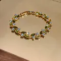 Vista macro dettagliata di un bracciale placcato oro con zirconi verdi e blu brillanti - Oro - Verde oliva