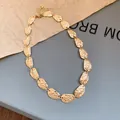 Vista detallada de un collar dorado con placas ovaladas de metal texturizado moderno. - Collar corto / Dorado