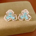 Macro view of blue zircon and resin flower stud earrings resting on a tan jewelry box - Flower Style (HE33995) / Silver Post - White - Blue
