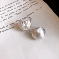 Detailed close-up of brushed silver semi-circular earrings resting on a vintage book page - Ear Buckle / Silver