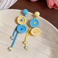 Vista detallada de pendientes coloridos estilo dopamina con colgantes de botones amarillos. - Pin de Plata 925 - Azul y Amarillo