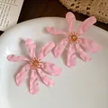 Detailed view of oversized pink matte flower earrings with golden stamen on a white plate - Pink / Silver Needle
