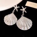 Detailed view of silver starfish and pleated shell drop earrings on a black background - Silver
