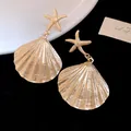 Close-up of gold metal starfish and pleated shell earrings on black background - Gold