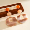 Close-up of geometric acrylic drop earrings with marble texture on wooden display - White-Coffee